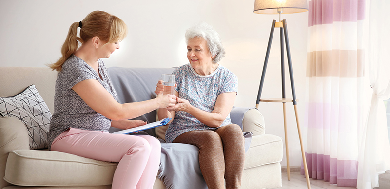 Pflegerin reicht Seniorin Wasser